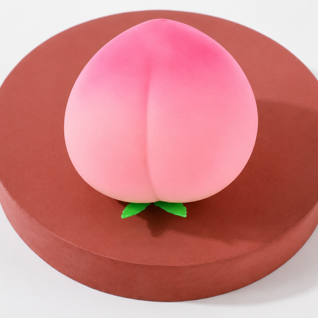 a pink ombré peach-shaped squishy toy with a soft touch texture, rounded fruit design, center groove, green leaf accent, and clear individual packaging