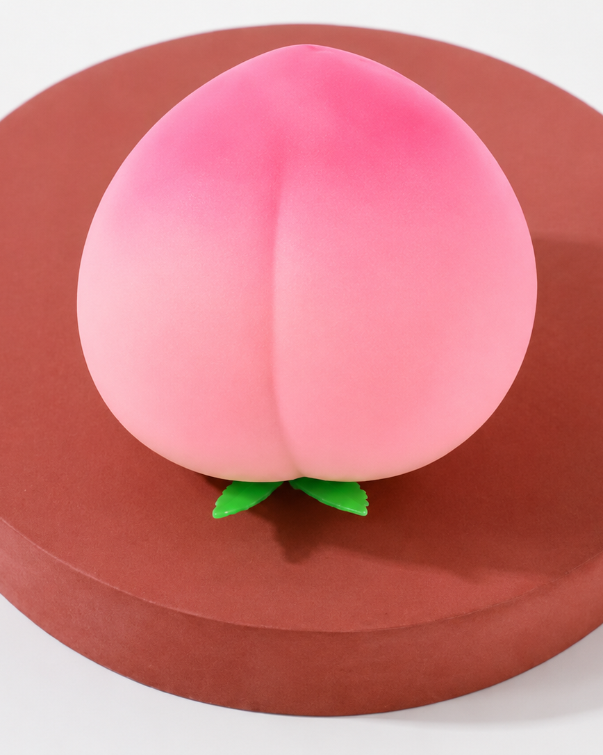 a pink ombré peach-shaped squishy toy with a soft touch texture, rounded fruit design, center groove, green leaf accent, and clear individual packaging