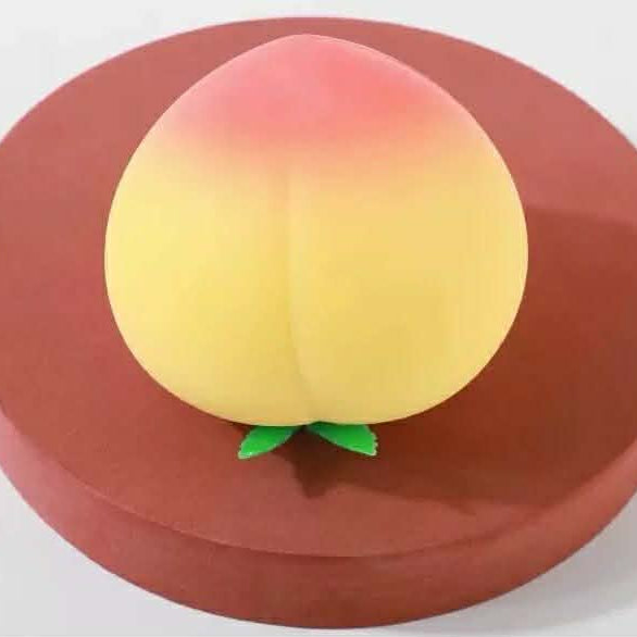 a yellow-orange ombré peach-shaped squishy toy with a soft touch texture, rounded fruit design, center groove, green leaf accent, and clear individual packaging