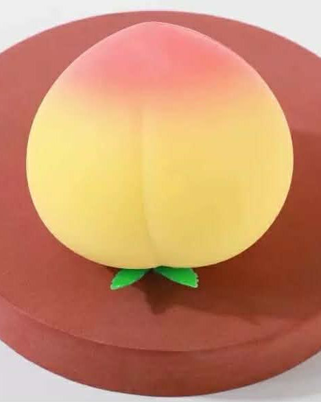 a yellow-orange ombré peach-shaped squishy toy with a soft touch texture, rounded fruit design, center groove, green leaf accent, and clear individual packaging