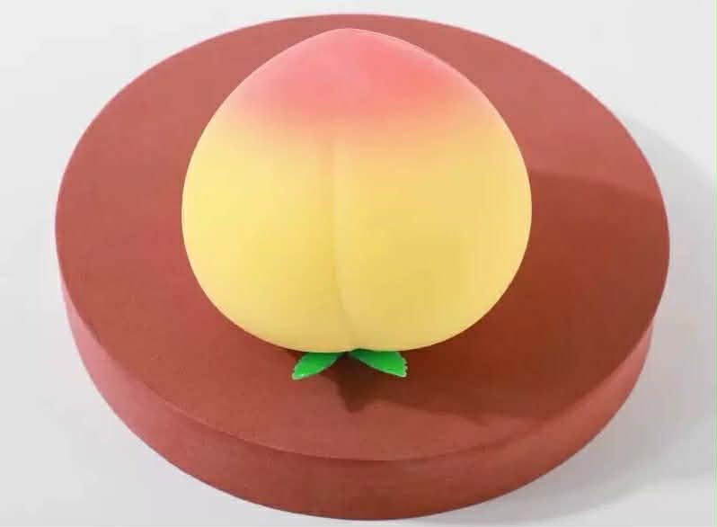 a yellow-orange ombré peach-shaped squishy toy with a soft touch texture, rounded fruit design, center groove, green leaf accent, and clear individual packaging