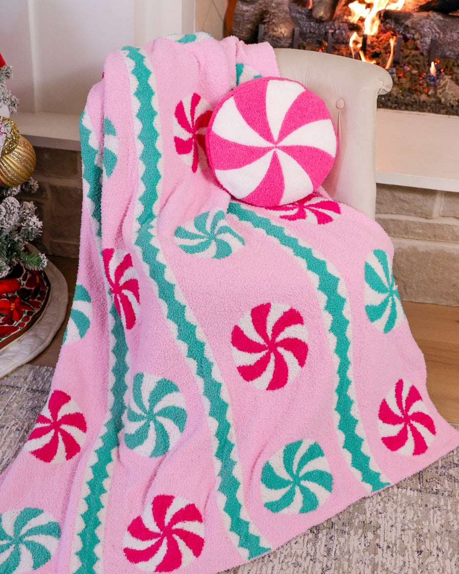 a round cushion with a bold hot pink and white peppermint swirl design on a soft, textured bouclé fabric paired with our Pink Wintermint Blanket