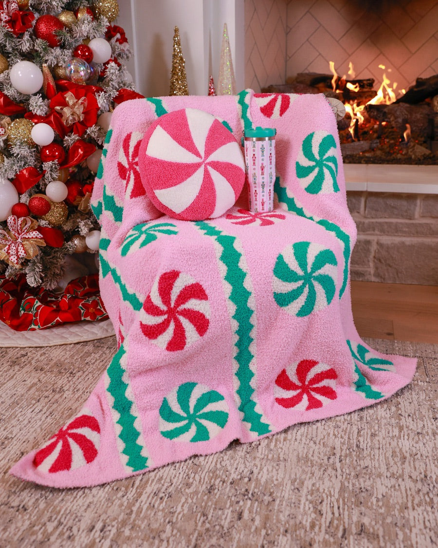 a round cushion with a bold hot pink and white peppermint swirl design on a soft, textured bouclé fabric paired with our Pink Wintermint Blanket and our Nutcracker Magic Travel Tumbler