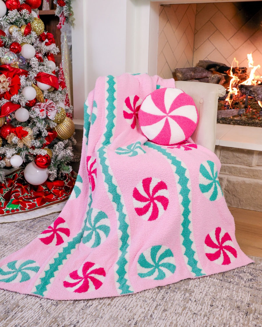 a round cushion with a bold hot pink and white peppermint swirl design on a soft, textured bouclé fabric paired with our Pink Wintermint Blanket