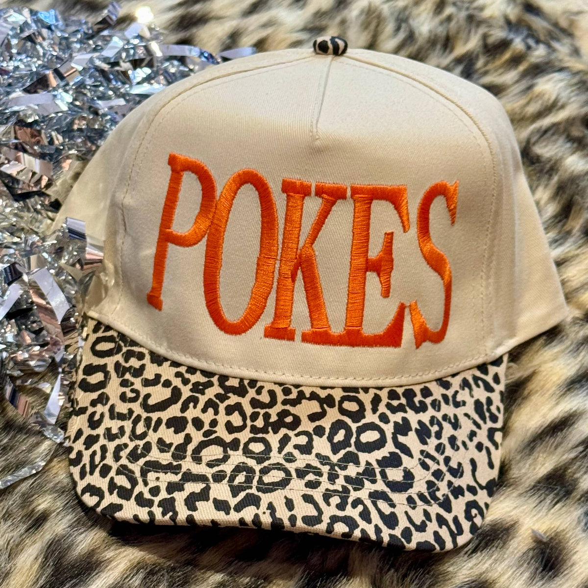 a lightweight unisex two-tone hat with embroidered orange 'POKES' lettering, cream structured front, curved contrasting black leopard bill, coordinating leopard top button, and adjustable snap-back closure