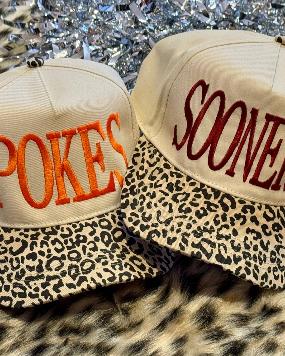 Two hats with 'POKES' and 'SOONERS' text on a leopard print background