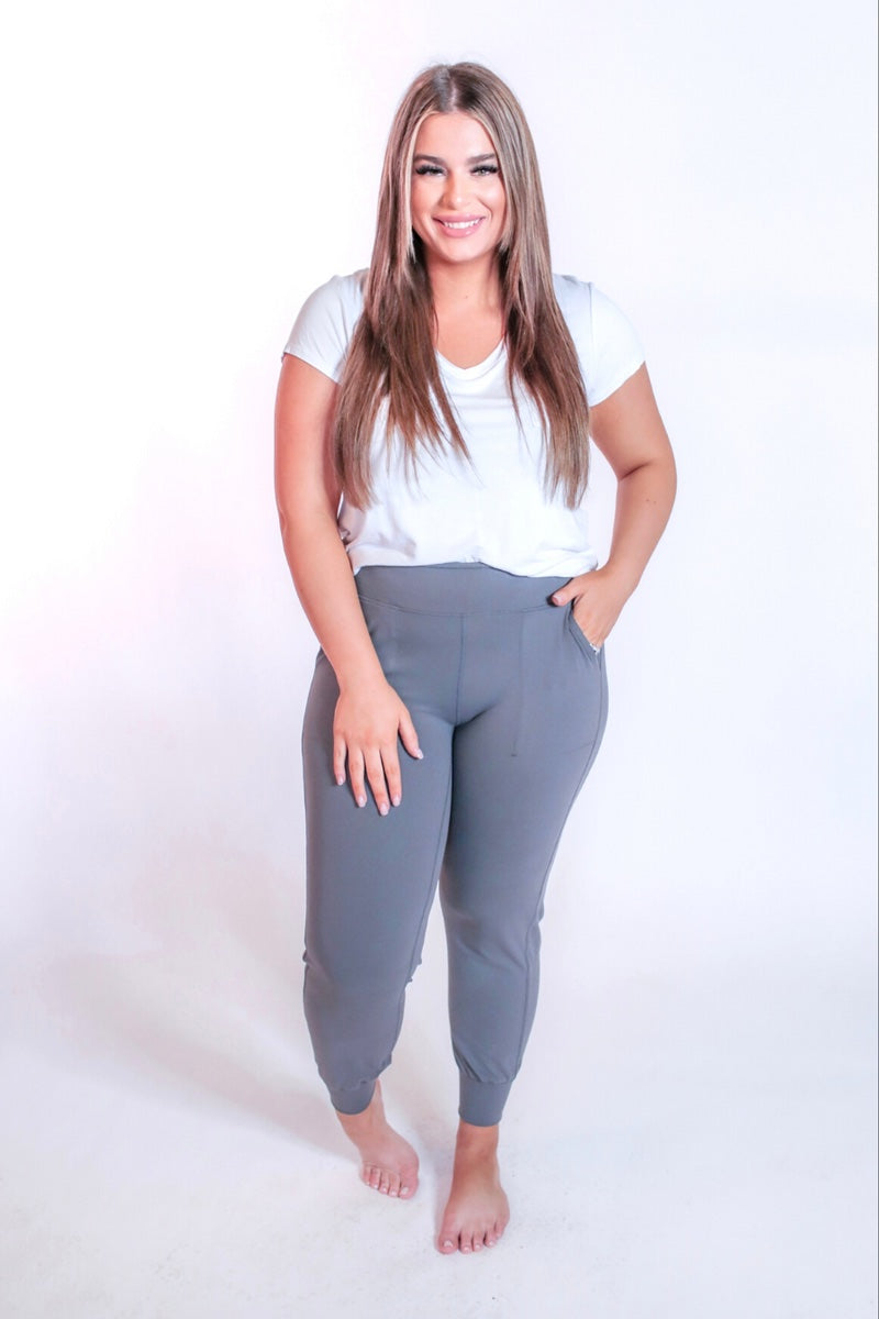 grey high-rise joggers crafted on smooth stretch fabric with a 3" waistband, side pockets, interior waistband back pocket, contoured back seam detail, tapered leg, and cuffed ankles