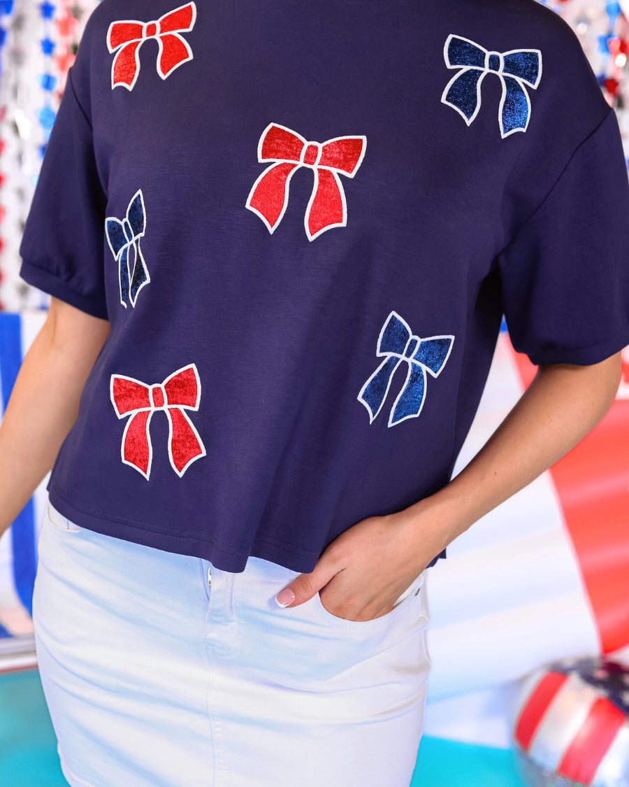 banded short-sleeved cropped fit luxe top with blue and red metallic foil bows outlined in white embroidery and side slits