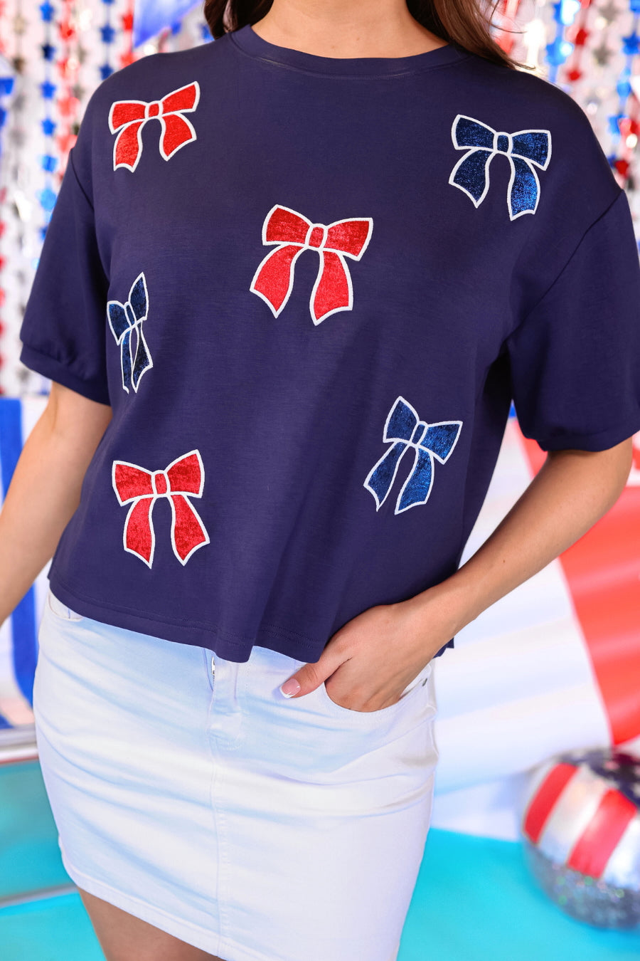 banded short-sleeved cropped fit luxe top with blue and red metallic foil bows outlined in white embroidery and side slits