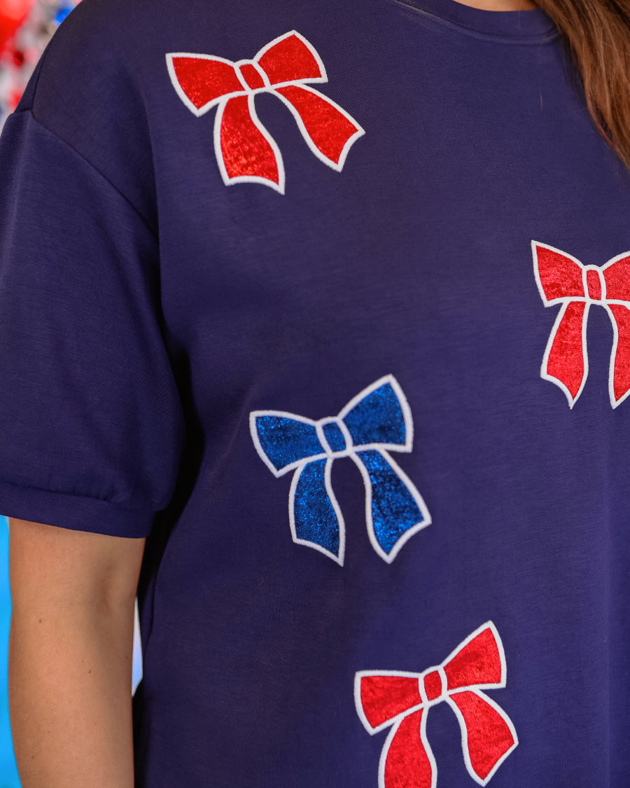 banded short-sleeved cropped fit luxe top with blue and red metallic foil bows outlined in white embroidery and side slits