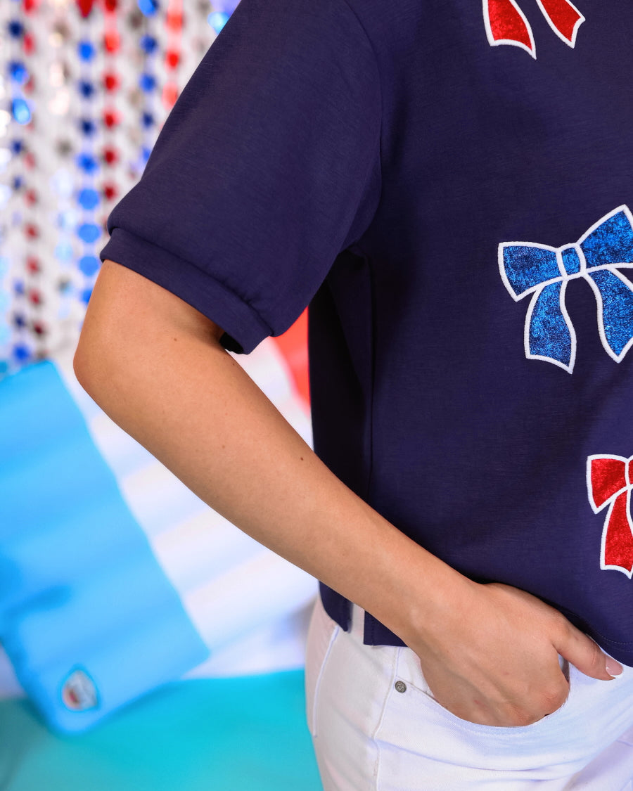 banded short-sleeved cropped fit luxe top with blue and red metallic foil bows outlined in white embroidery and side slits