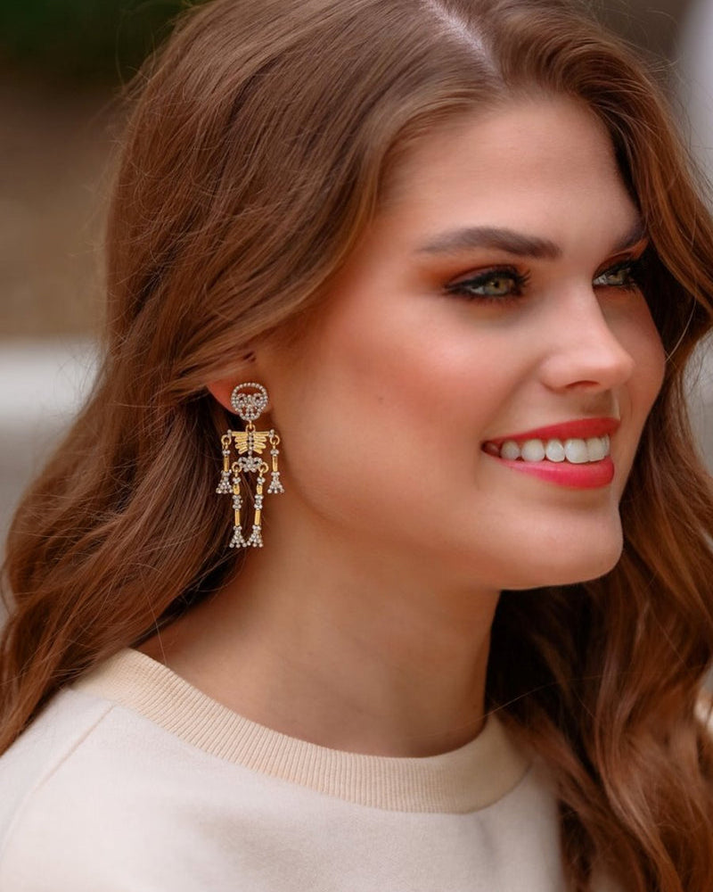 gold-plated post-back skeleton-shaped dangle earrings with rhinestone accents, skull stud tops, articulated bone design, matching barrel backs, and nickel/lead compliant construction in gold