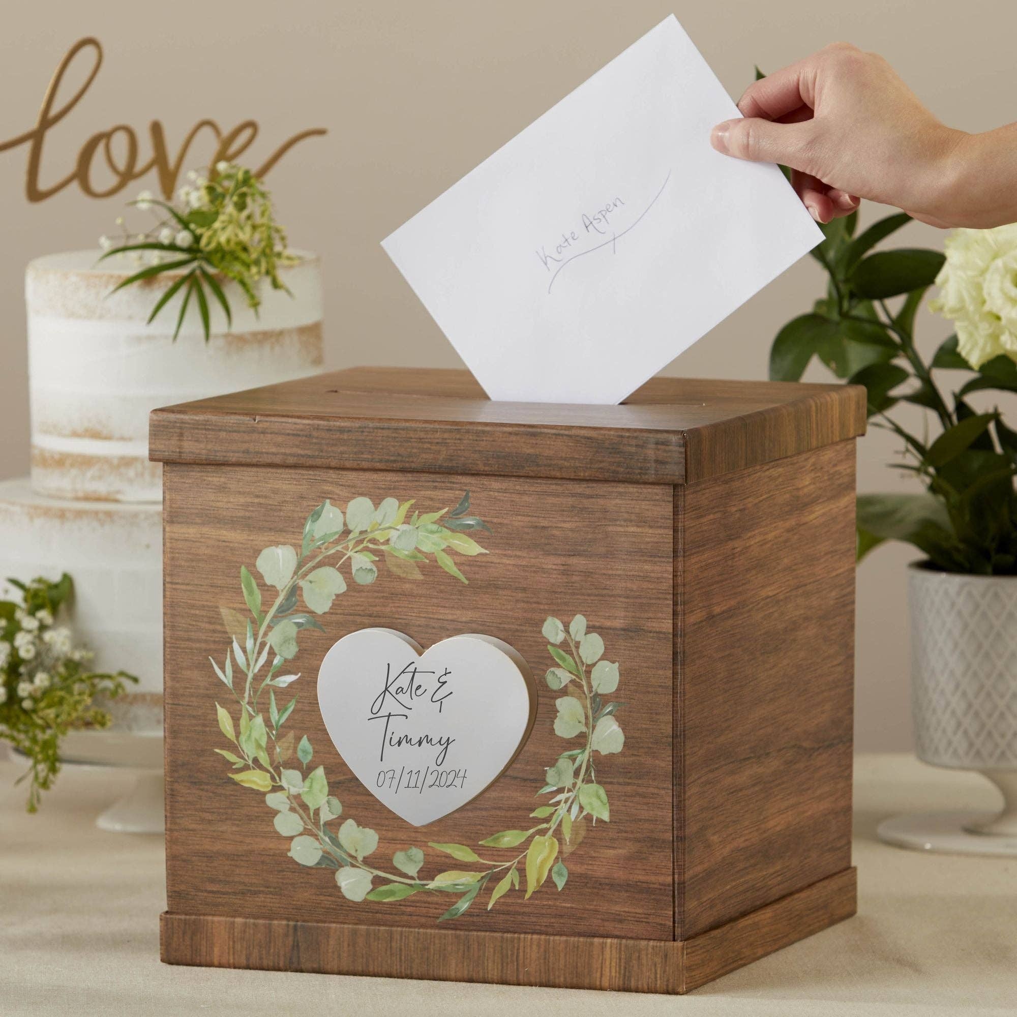 Wooden card box with decorative heart and foliage design, being opened with a card inside, against a wedding-themed background.