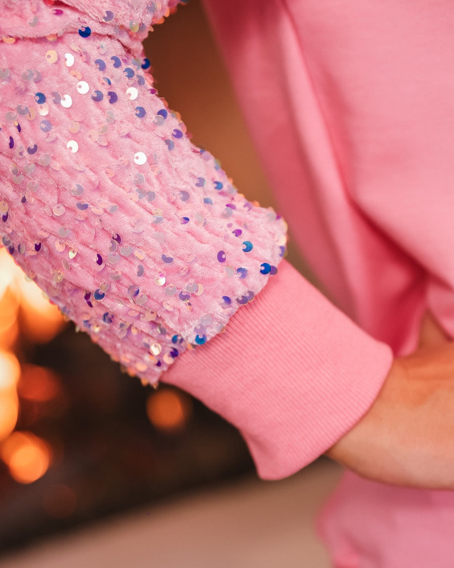 a lightweight pink long-sleeve top decorated with four vibrant nutcracker designs finished with dimensional beaded effect boots and accented by soft, shimmering velvet-sequin sleeves, a relaxed drop shoulder, and ribbed crew neckline, cuffs, and hem