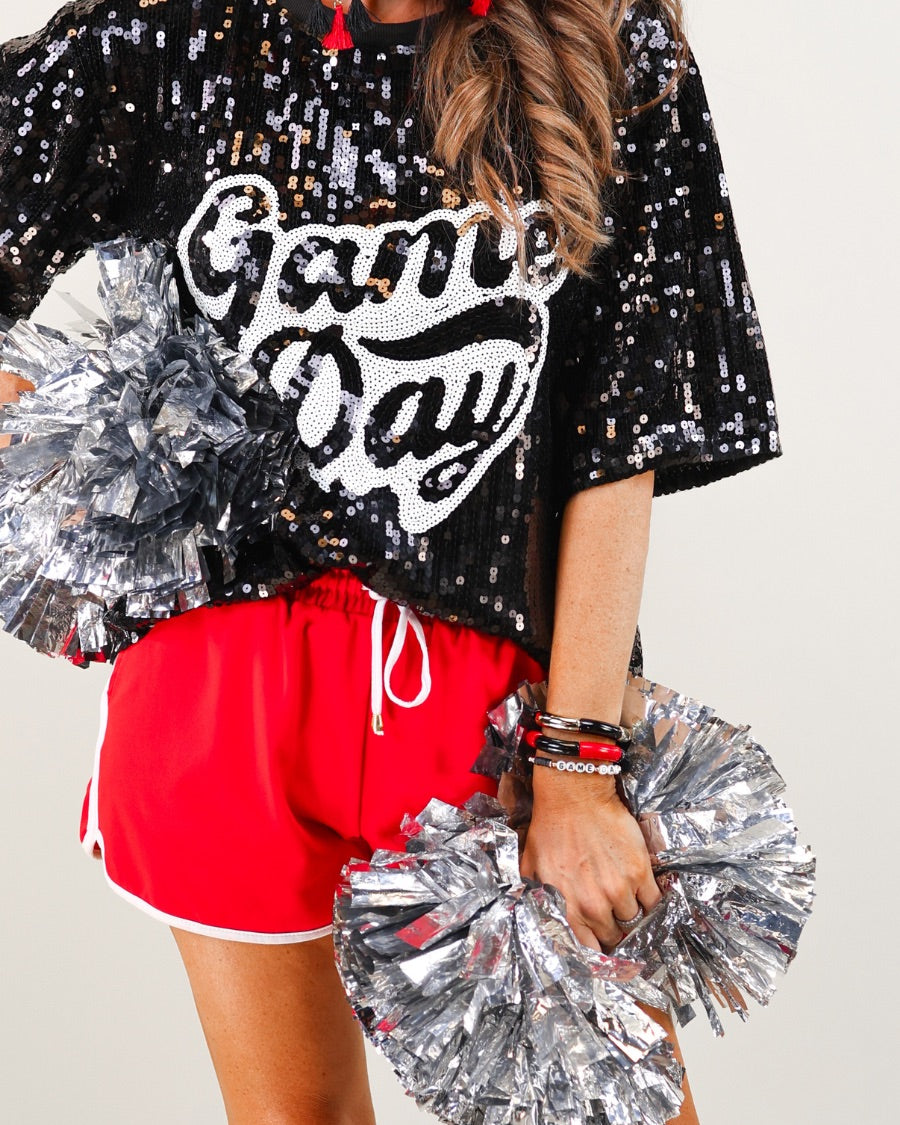 a full sequin design top on a solid color with the words 'Game Day" on the center front outlined in white sequins, a boxy fit, and a lined interior in black