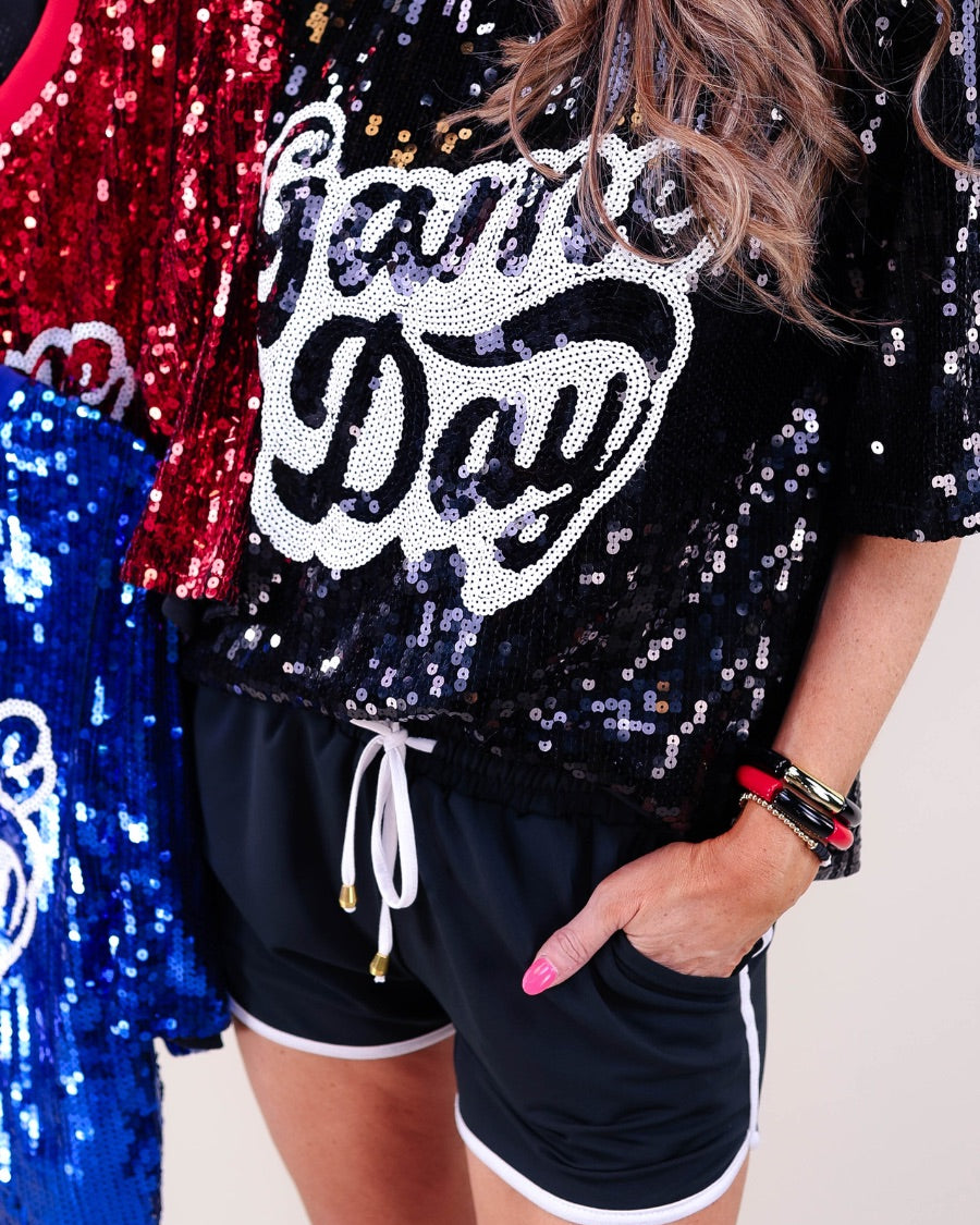 a full sequin design top on a solid color with the words 'Game Day" on the center front outlined in white sequins, a boxy fit, and a lined interior in black, red, and royal blue