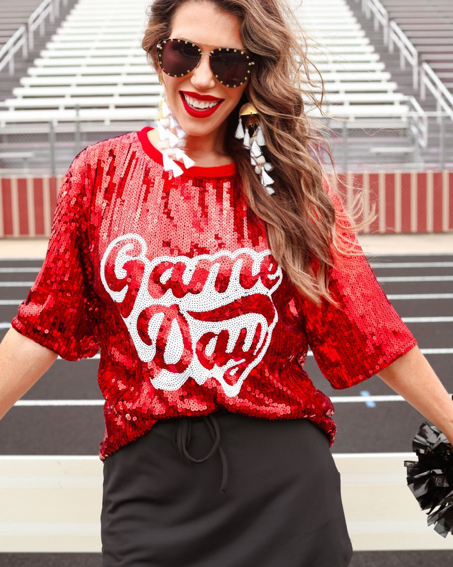 a full sequin design top on a solid color with the words 'Game Day" on the center front outlined in white sequins, a boxy fit, and a lined interior in red