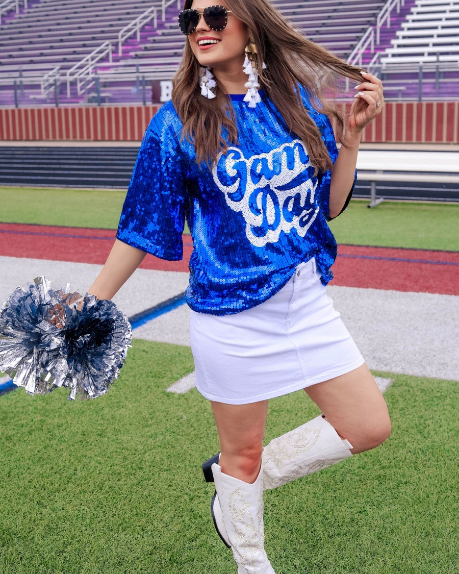 a full sequin design top on a solid color with the words 'Game Day" on the center front outlined in white sequins, a boxy fit, and a lined interior in royal blue