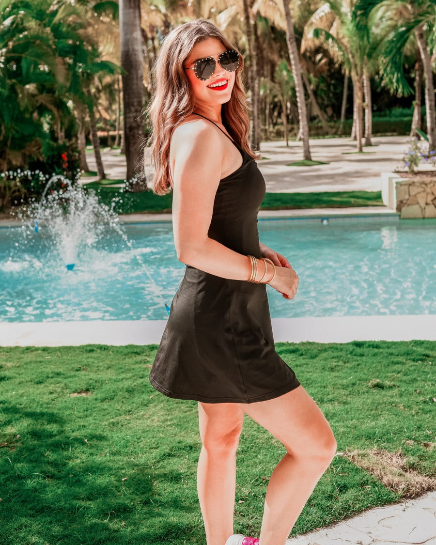 a black sleeveless tennis dress designed with built-in shorts featuring hidden side pockets, adjustable crisscross straps, and built-in shelf bra