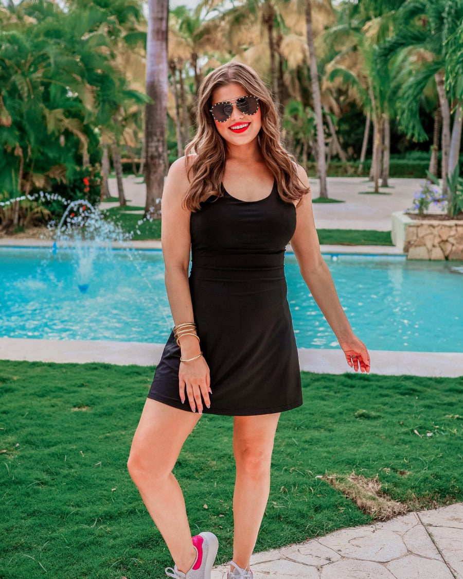 a black sleeveless tennis dress designed with built-in shorts featuring hidden side pockets, adjustable crisscross straps, and built-in shelf bra