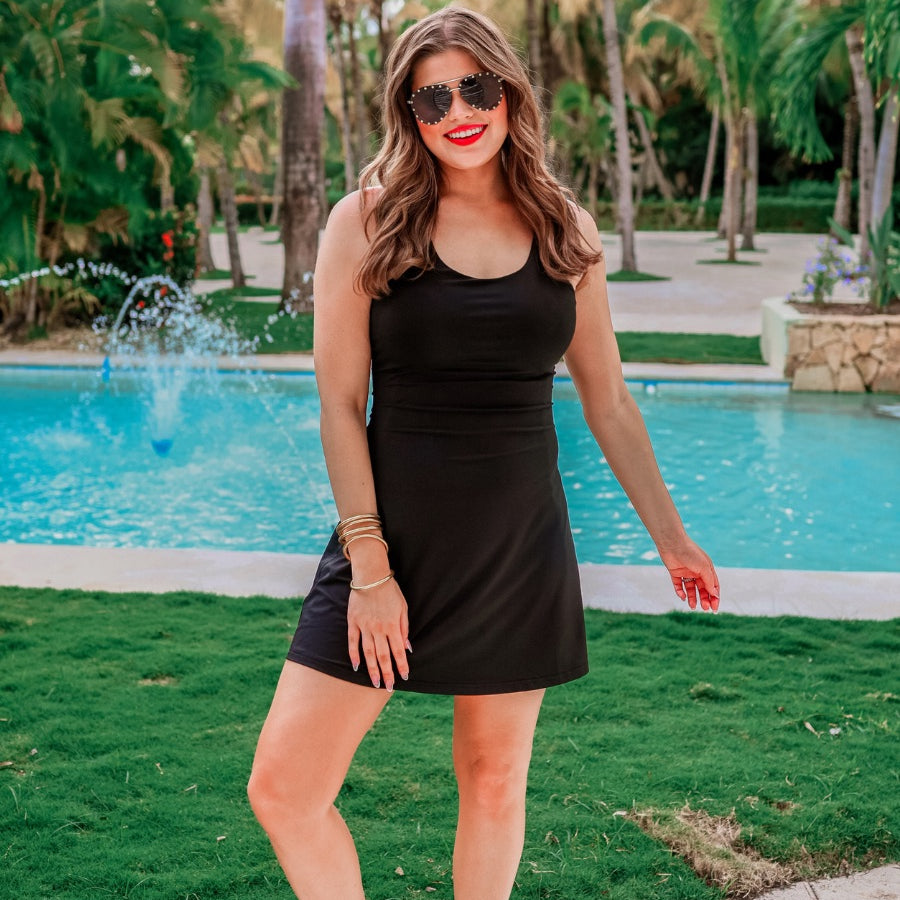 a black sleeveless tennis dress designed with built-in shorts featuring hidden side pockets, adjustable crisscross straps, and built-in shelf bra