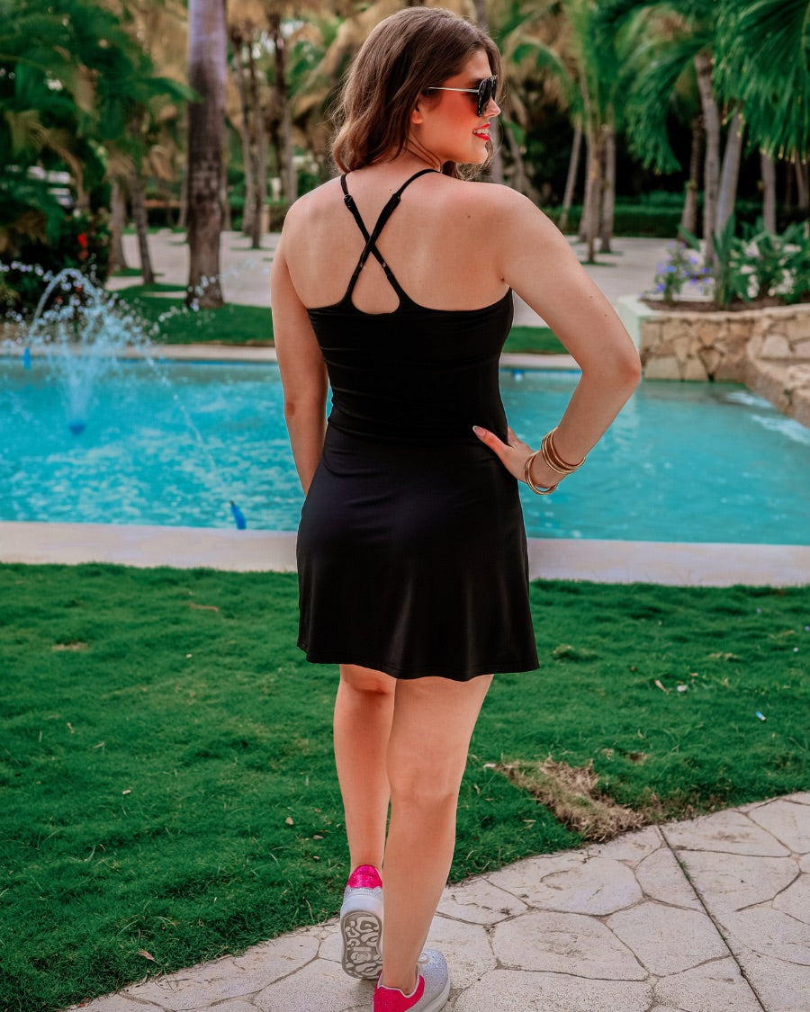 a black sleeveless tennis dress designed with built-in shorts featuring hidden side pockets, adjustable crisscross straps, and built-in shelf bra