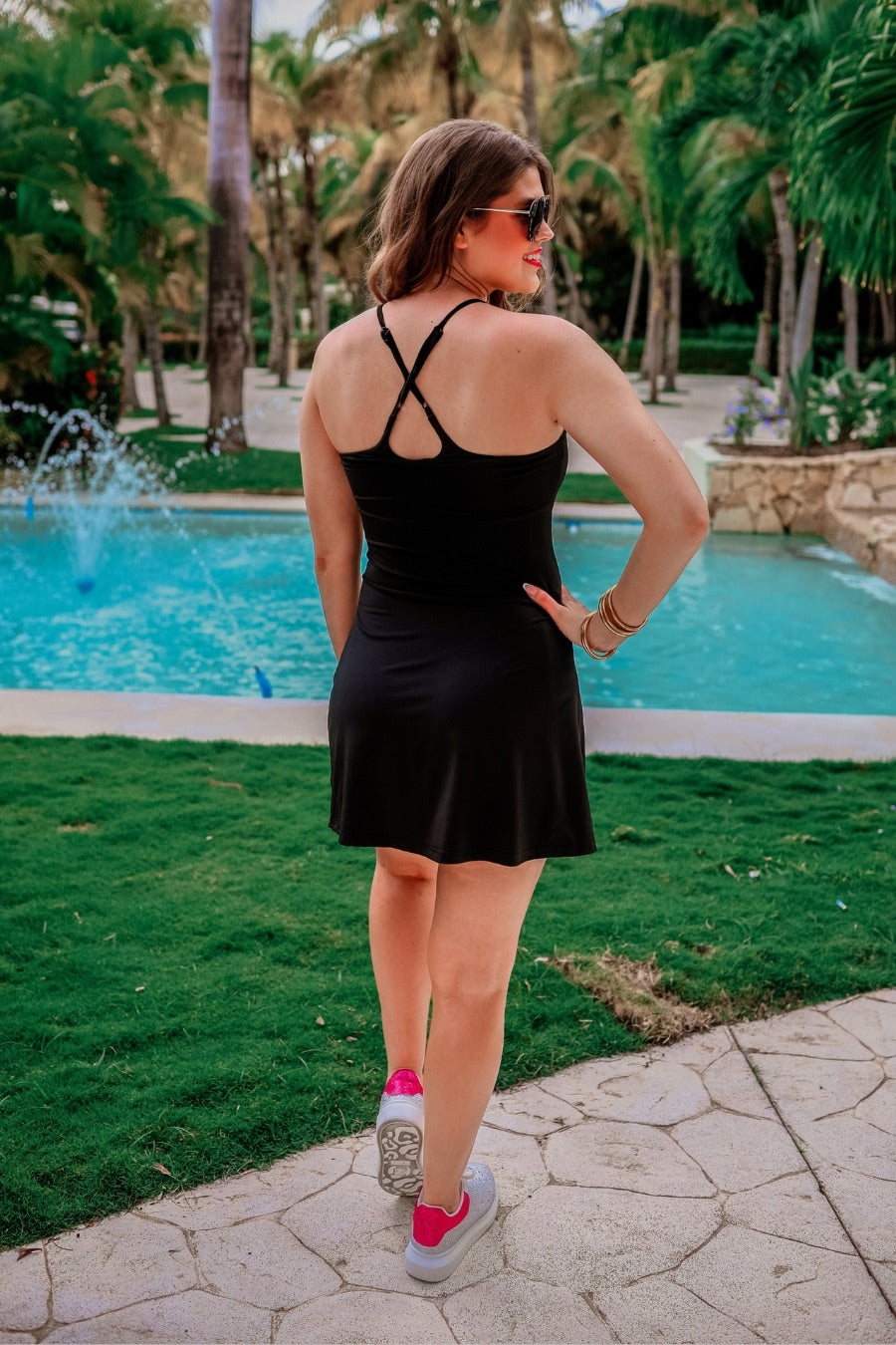 a black sleeveless tennis dress designed with built-in shorts featuring hidden side pockets, adjustable crisscross straps, and built-in shelf bra