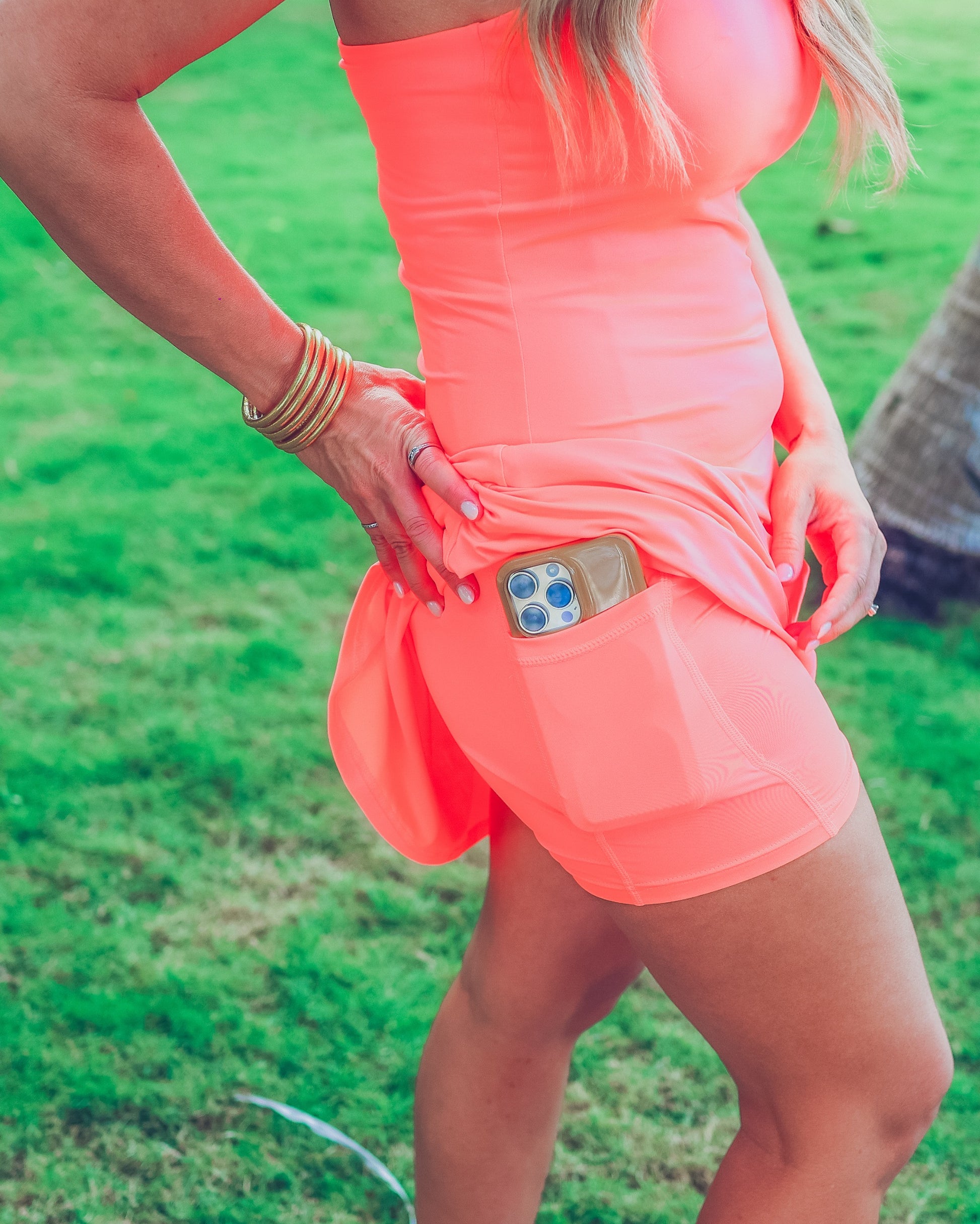 a coral sleeveless tennis dress designed with built-in shorts featuring hidden side pockets, adjustable crisscross straps, and built-in shelf bra