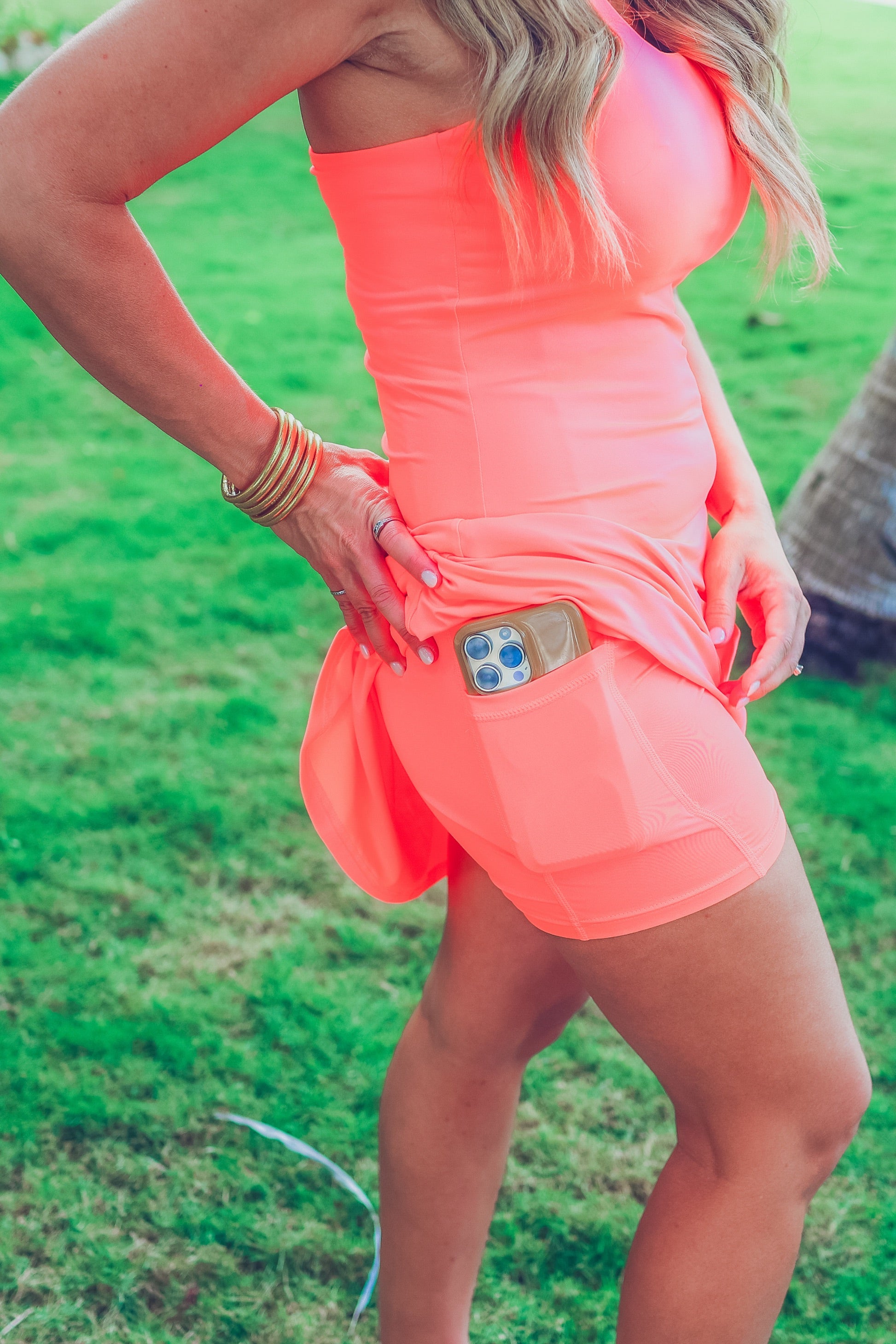 a coral sleeveless tennis dress designed with built-in shorts featuring hidden side pockets, adjustable crisscross straps, and built-in shelf bra