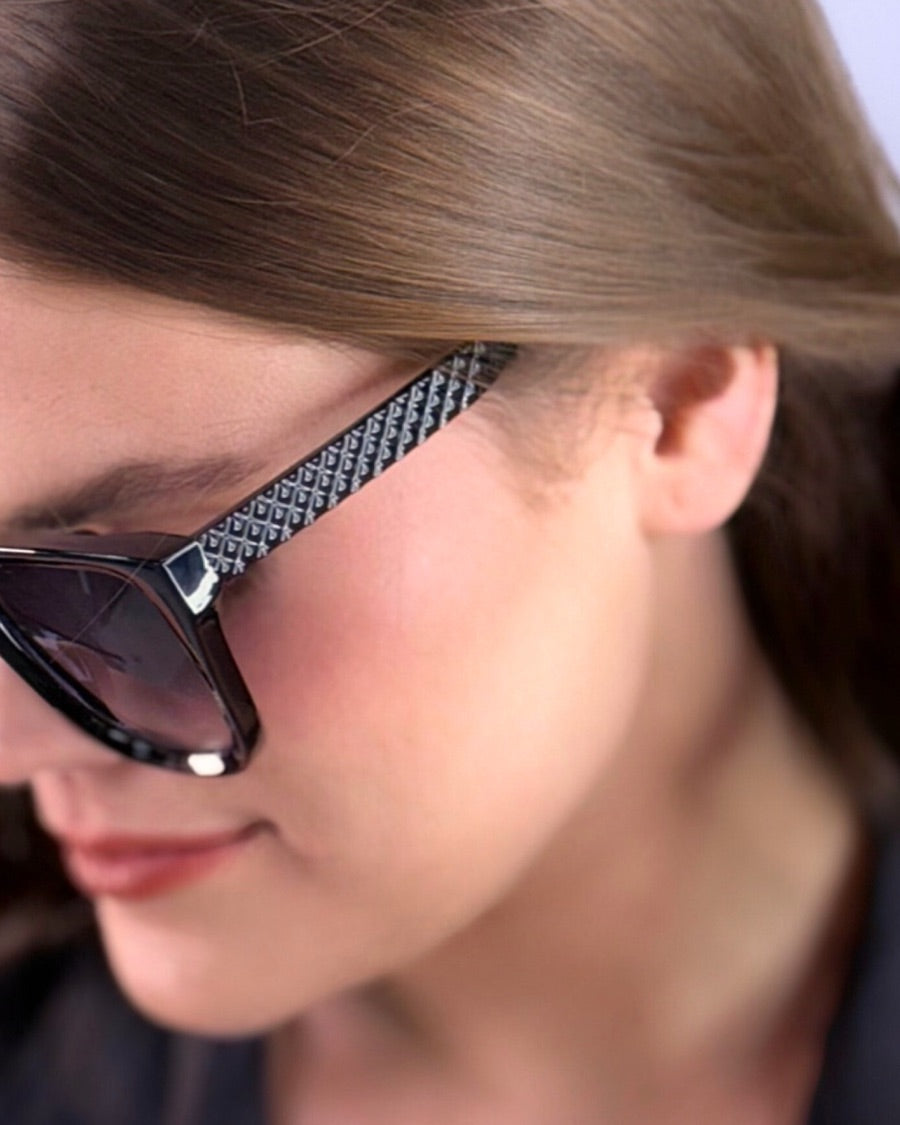 oversized square sunglasses in black with dark lenses, a raised geometric texture on the temples, and brand name detail (on both the temple and the complimentary black pouch)
