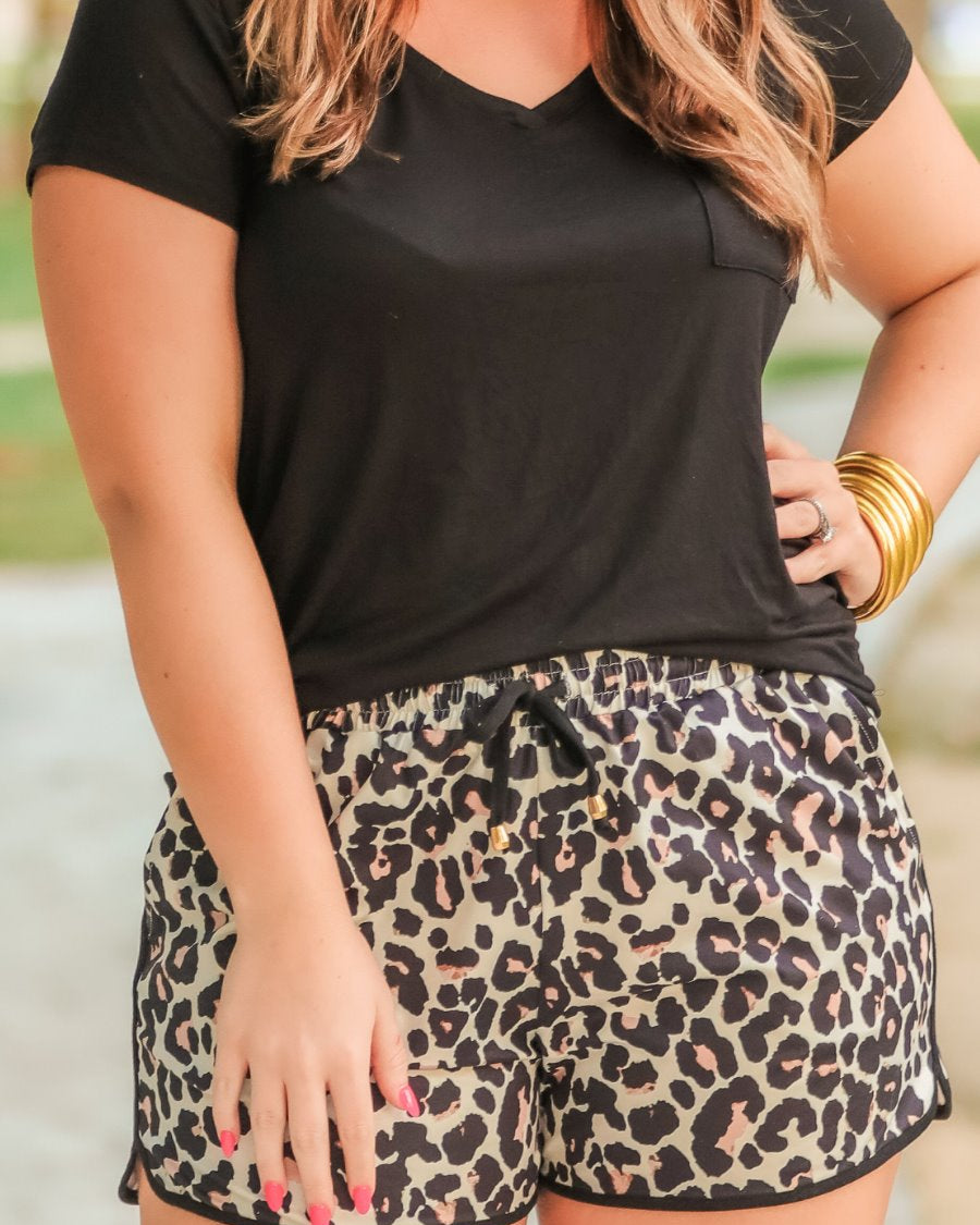 mid-rise relaxed fit activewear shorts with side pockets and a tie waist drawstring with gold bead accents, designed on a black and brown leopard pattern print fabric, tan base, and black trim