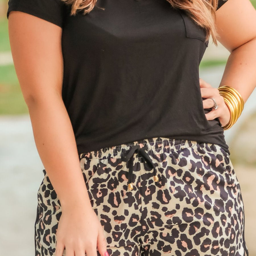 mid-rise relaxed fit activewear shorts with side pockets and a tie waist drawstring with gold bead accents, designed on a black and brown leopard pattern print fabric, tan base, and black trim
