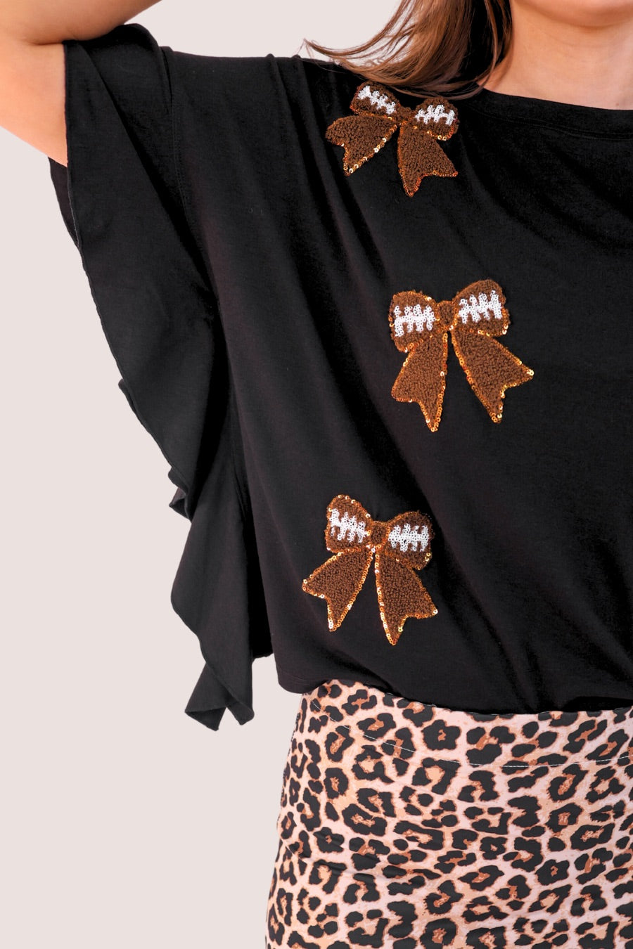 fluttery ruffle short-sleeve top with a mom crop length, sewn-on chenille football bow patches outlined in sequins on a soft, stretch-knit fabric in black