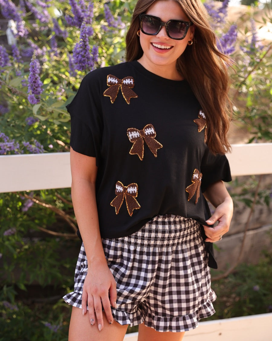 fluttery ruffle short-sleeve top with a mom crop length, sewn-on chenille football bow patches outlined in sequins on a soft, stretch-knit fabric in black