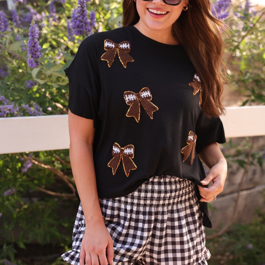 fluttery ruffle short-sleeve top with a mom crop length, sewn-on chenille football bow patches outlined in sequins on a soft, stretch-knit fabric in black