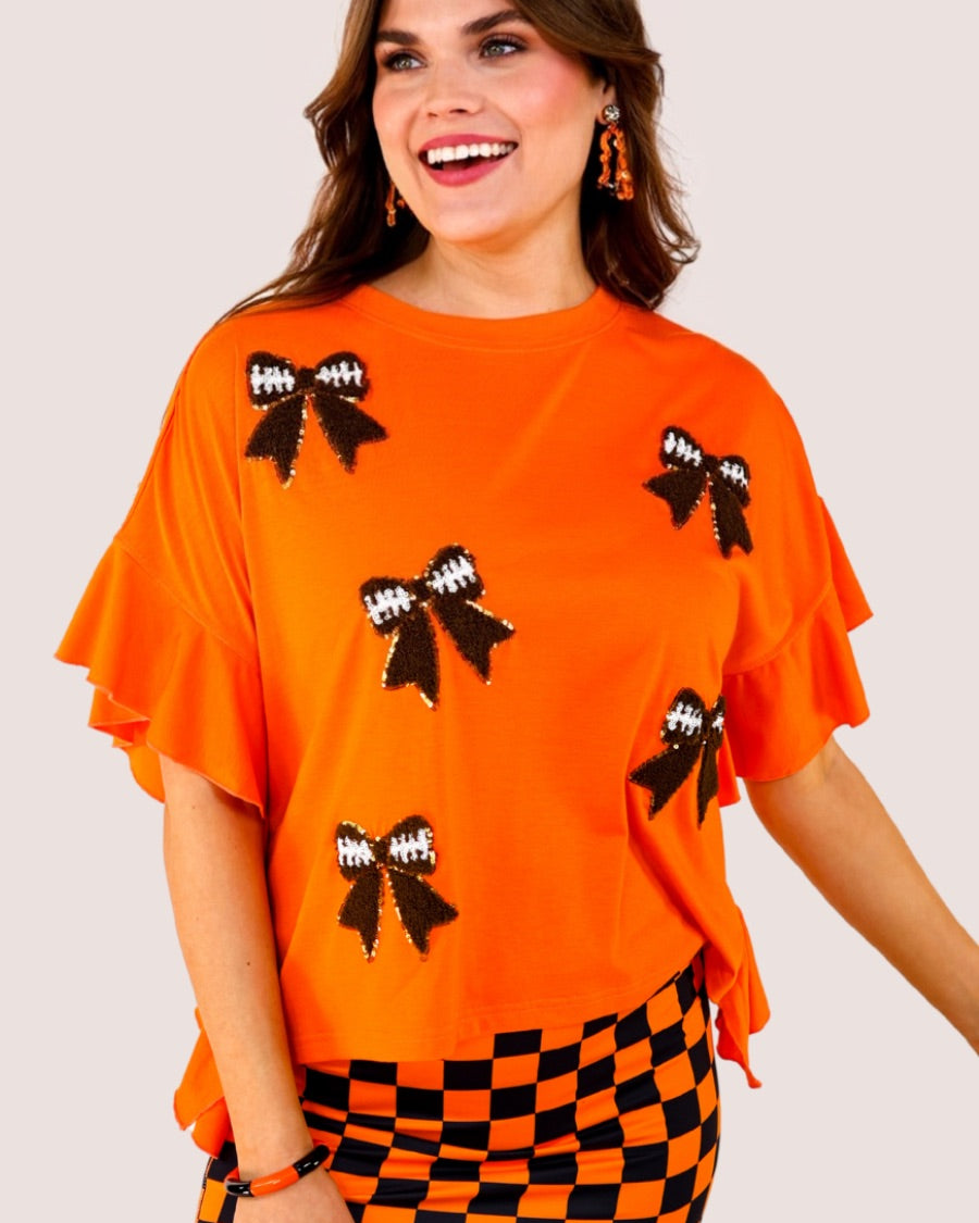 fluttery ruffle short-sleeve top with a mom crop length, sewn-on chenille football bow patches outlined in sequins on a soft, stretch-knit fabric in orange