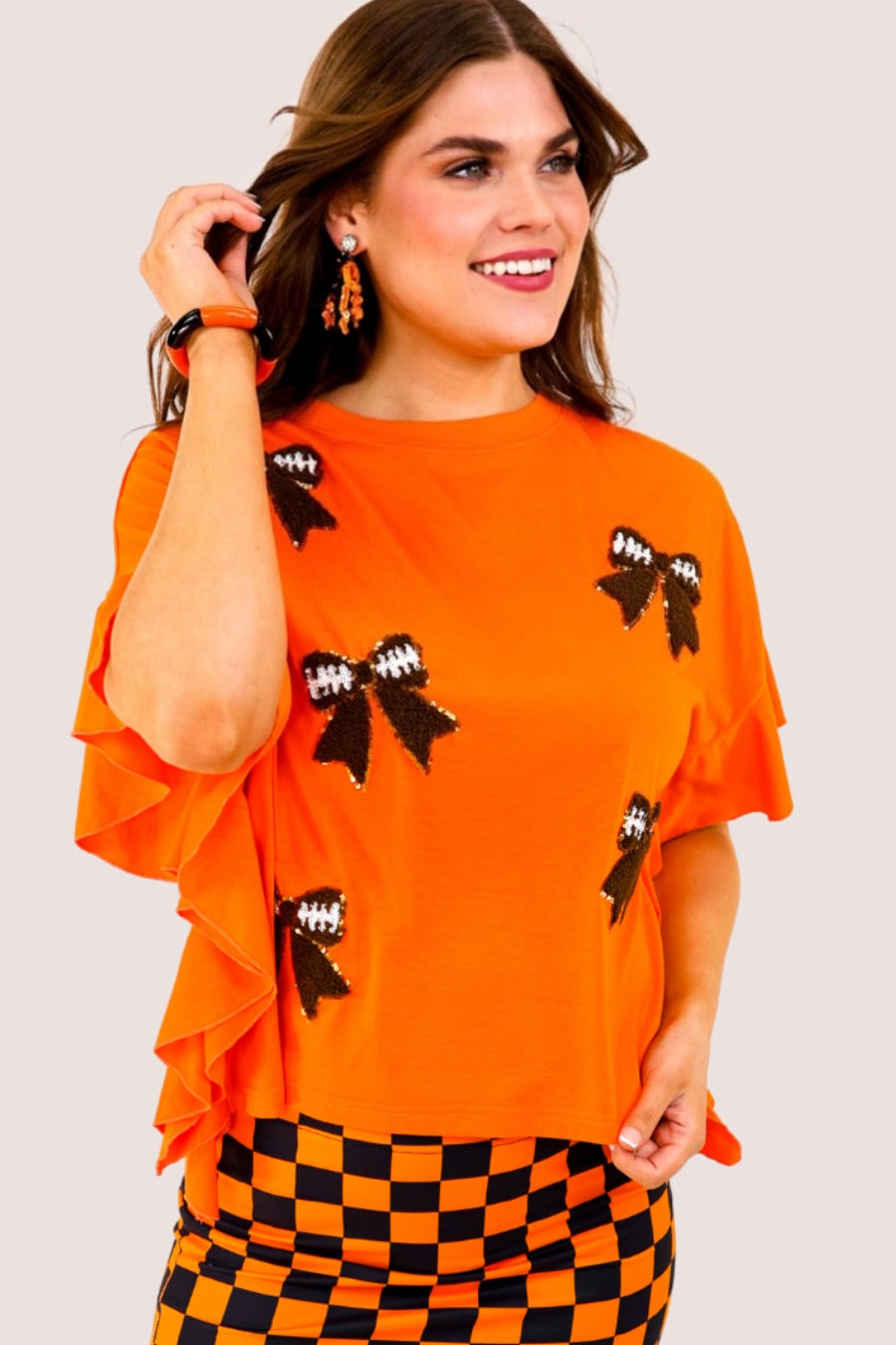 fluttery ruffle short-sleeve top with a mom crop length, sewn-on chenille football bow patches outlined in sequins on a soft, stretch-knit fabric in orange