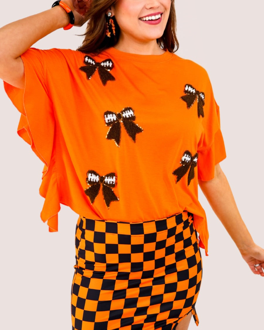 fluttery ruffle short-sleeve top with a mom crop length, sewn-on chenille football bow patches outlined in sequins on a soft, stretch-knit fabric in orange