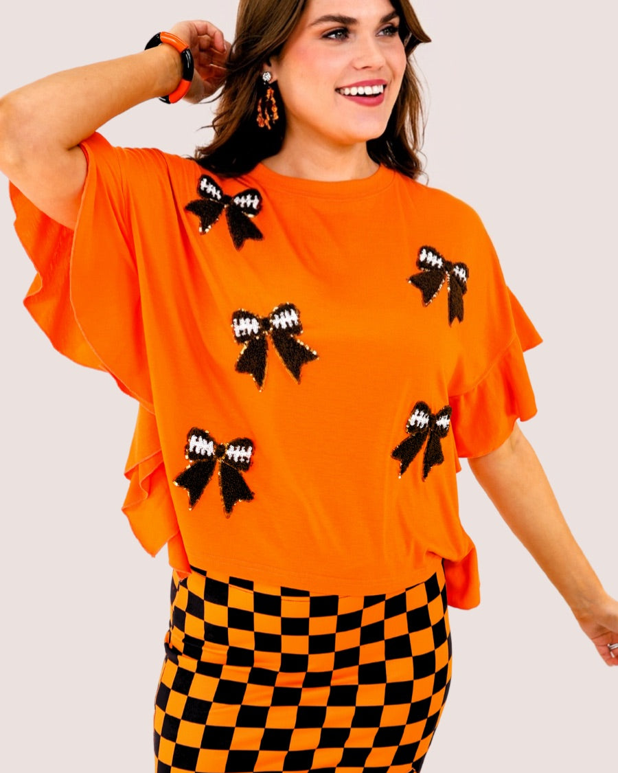 fluttery ruffle short-sleeve top with a mom crop length, sewn-on chenille football bow patches outlined in sequins on a soft, stretch-knit fabric in orange