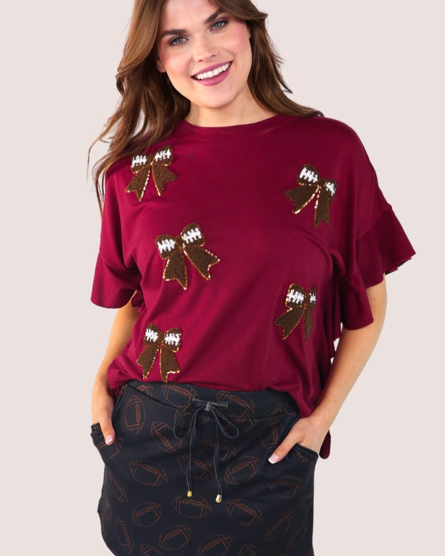 fluttery ruffle short-sleeve top with a mom crop length, sewn-on chenille football bow patches outlined in sequins on a soft, stretch-knit fabric in maroon