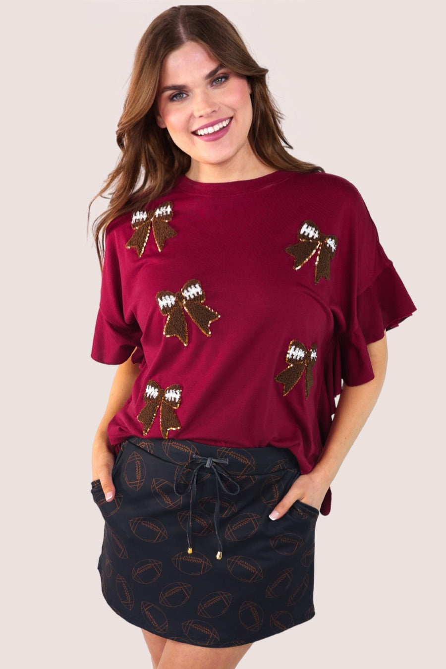 fluttery ruffle short-sleeve top with a mom crop length, sewn-on chenille football bow patches outlined in sequins on a soft, stretch-knit fabric in maroon