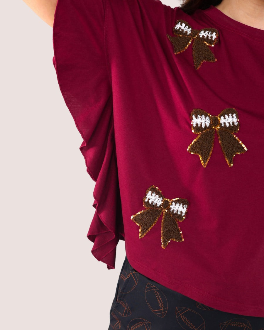 fluttery ruffle short-sleeve top with a mom crop length, sewn-on chenille football bow patches outlined in sequins on a soft, stretch-knit fabric in maroon