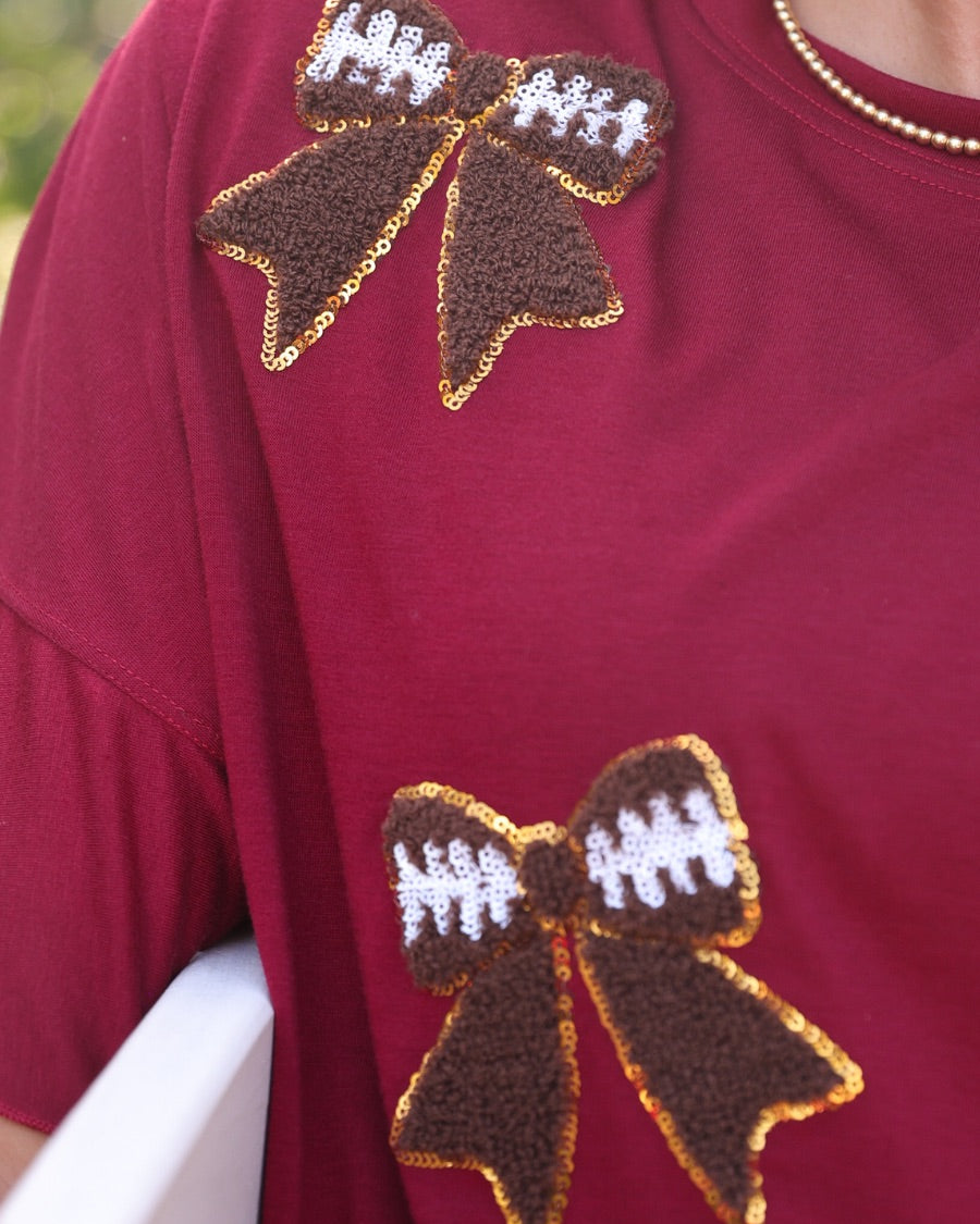 fluttery ruffle short-sleeve top with a mom crop length, sewn-on chenille football bow patches outlined in sequins on a soft, stretch-knit fabric in maroon
