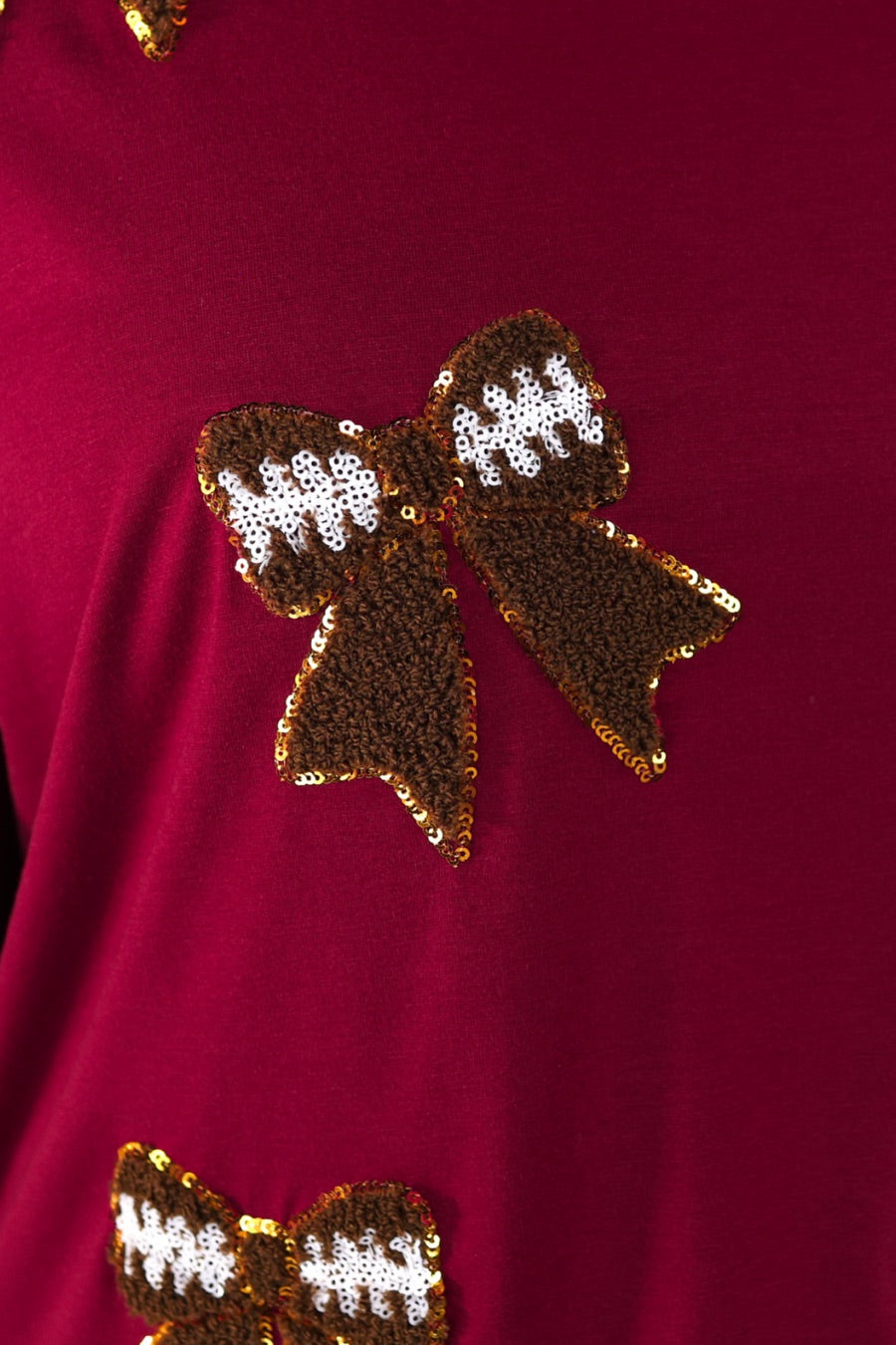 fluttery ruffle short-sleeve top with a mom crop length, sewn-on chenille football bow patches outlined in sequins on a soft, stretch-knit fabric in maroon