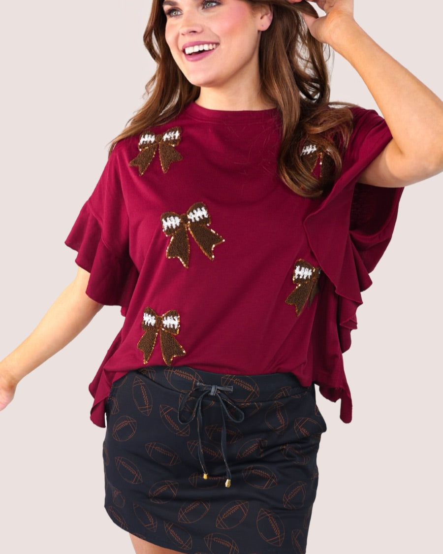 fluttery ruffle short-sleeve top with a mom crop length, sewn-on chenille football bow patches outlined in sequins on a soft, stretch-knit fabric in maroon
