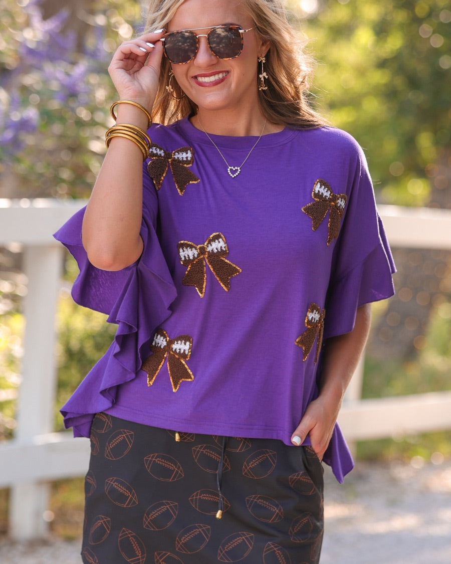 fluttery ruffle short-sleeve top with a mom crop length, sewn-on chenille football bow patches outlined in sequins on a soft, stretch-knit fabric in purple
