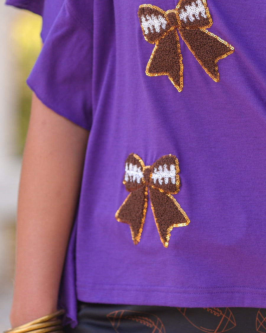 fluttery ruffle short-sleeve top with a mom crop length, sewn-on chenille football bow patches outlined in sequins on a soft, stretch-knit fabric in purple