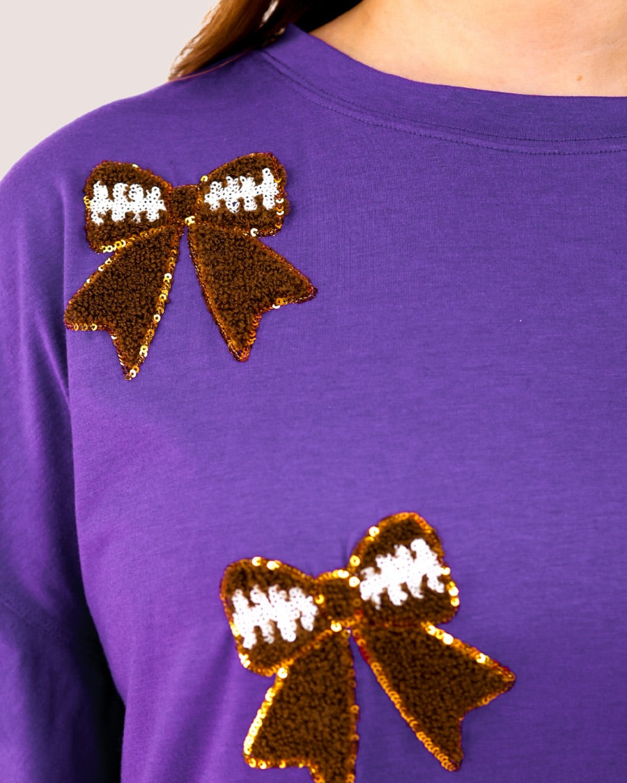 fluttery ruffle short-sleeve top with a mom crop length, sewn-on chenille football bow patches outlined in sequins on a soft, stretch-knit fabric in purple