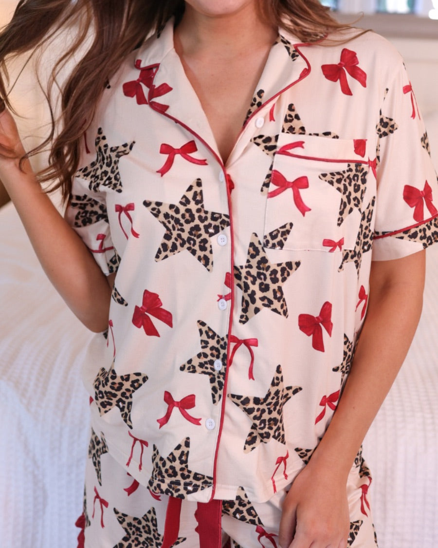 short-sleeve button-down style top with contrast piping and a chest pocket, paired with matching ruffle-trimmed shorts with an elastic waist and decorative tie, designed on a leopard star and red bow pattern print and a cream base, crafted on a soft, lightweight stretchy fabric