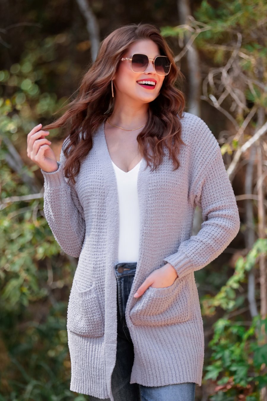 long-sleeve cardigan made of a soft knit material with front pockets and a draped open front silhouette that ends in a straight hemline on a grey fabric